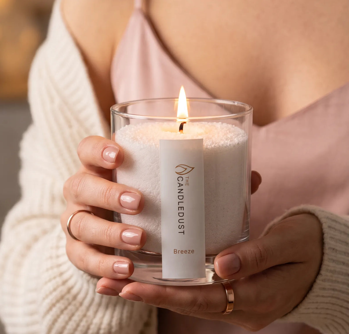 A Woman holds a lit Candledust Breeze scented pearled candle in a 160g glass jar
