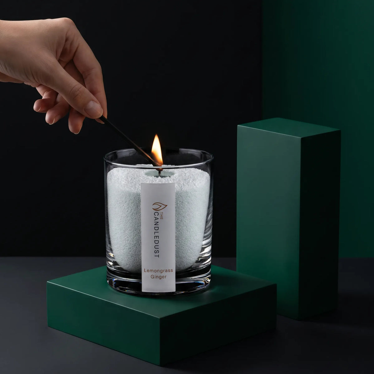 Close-up of a woman's hand lighting the cotton wick of a Lemongrass Ginger scented pearled sand candle in glass