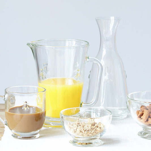 Clear La Rochère Bee glass jug filled with fresh orange juice, placed on a set morning breakfast table