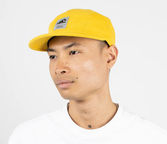 Model wearing the bright yellow Moomin Stinky 5-panel cap on a clean background
