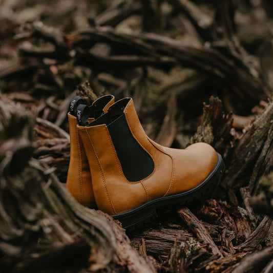 Side view of brown KIRA 3.0 Chelsea Boots resting on the natural forest floor, crafted from sustainable vegan leather.