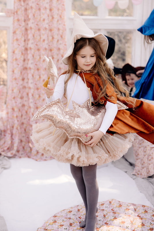 a joyful girl dressed in a costume, celebrating, with a vibrant floral Spring Garden Organic Cotton Canopy behind her as a magical backdrop