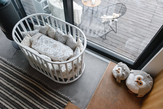 Round Baby Crib OLIN with Mattress - White in the bedroom near the window. with soft toys on the floor.