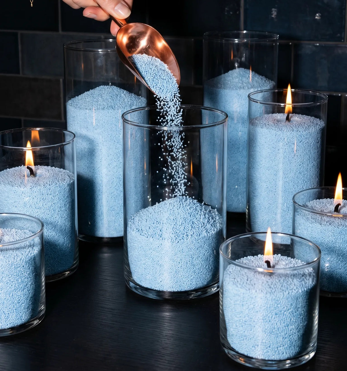 Close up of Woman's hand filling decorative glass candle holders with Sky Blue natural pearled candle sand