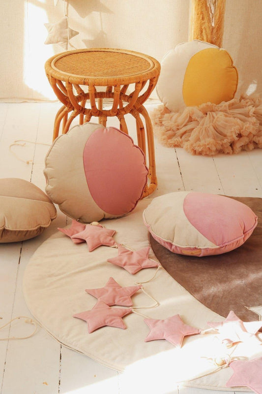 Scandi nursery decor: a Moi Mili Soft Pink Dust Star Garland resting on a woven cotton playmat over a beautiful natural wood floor in a cozy room corner