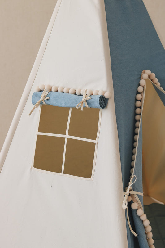 Nursery detail: close-up of the side window on a Moi Mili Jeans Teepee Tent, showing the contrast between blue denim and cream pompom trim
