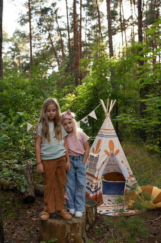Forest adventure: a happy child playing with small wooden toys inside a play tent, sitting comfortably on a Moi Mili Native Vibe Round Cotton Mat in the middle of a pine woods