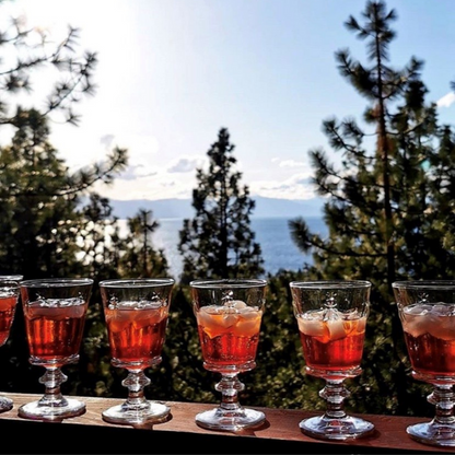 A lifestyle photograph of multiple La Rochere Bee glasses filled with ice and drinks (on the rocks) on a terrace, with a breathtaking mountain range and clear sky in the background.