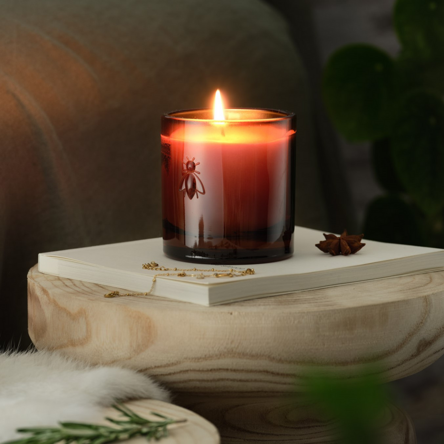 Close up of a glowing lit La Rochère Orange Blossom bee candle placed on a side table next to a sofa