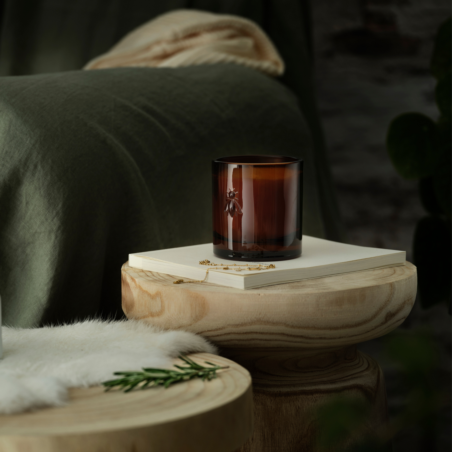 Cozy home decor scene with an unlit La Rochère Orange Blossom bee candle resting on a book next to a living room sofa