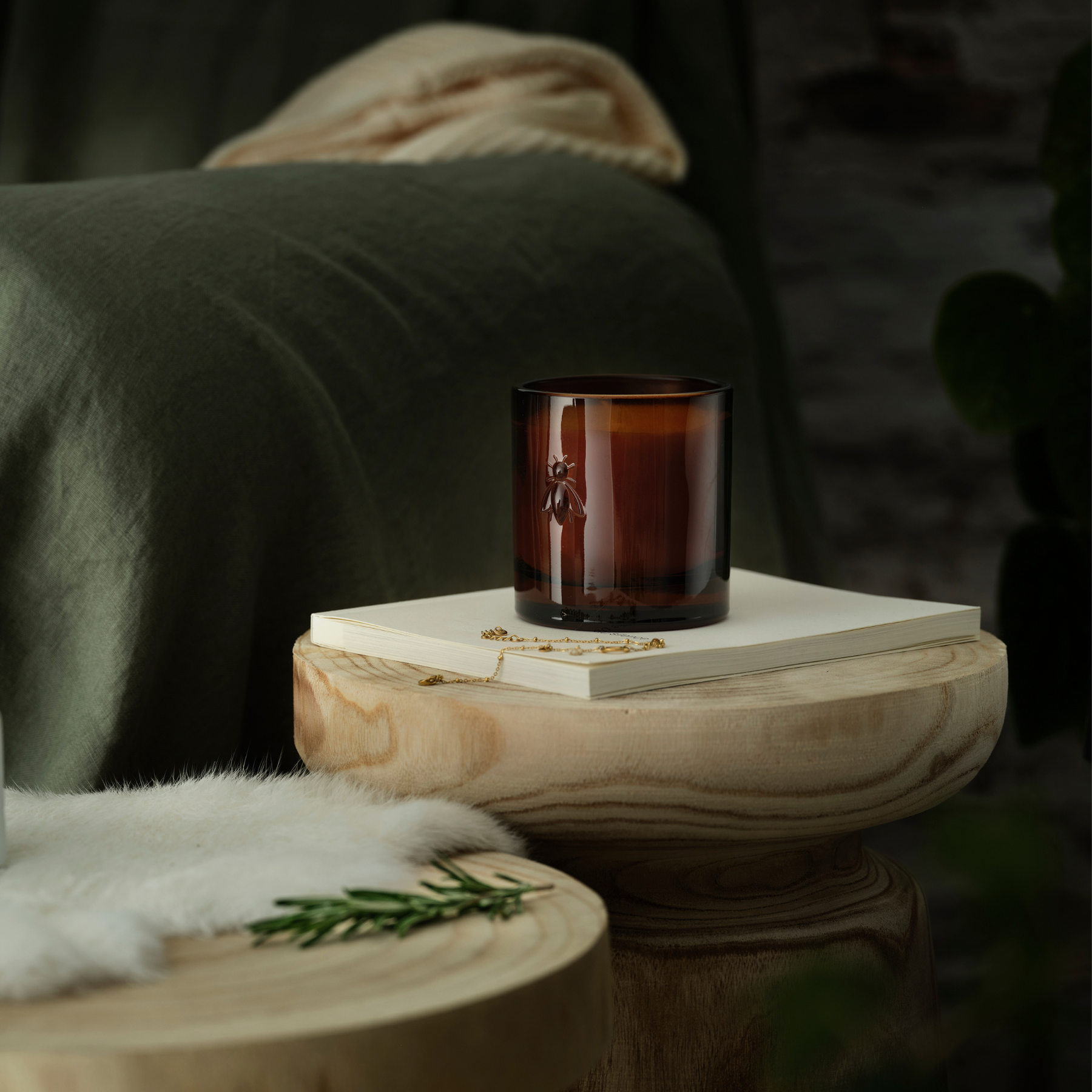 Cozy home decor scene with an unlit La Rochère Orange Blossom bee candle resting on a book next to a living room sofa