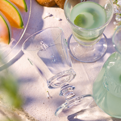 Detailed close-up of a single La Rochère Bee glass inverted on an outdoor table, with fresh melon slices visible next to it