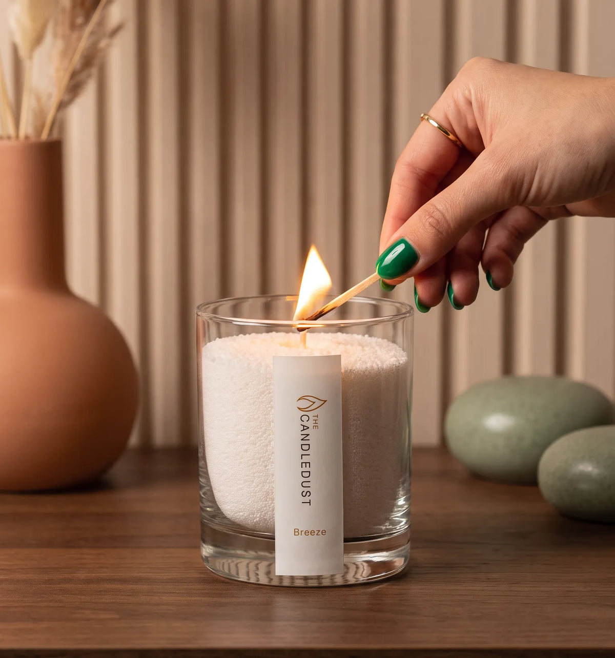 Close-up of a woman's hand lighting the cotton wick of a Breeze scented pearled sand candle in glass