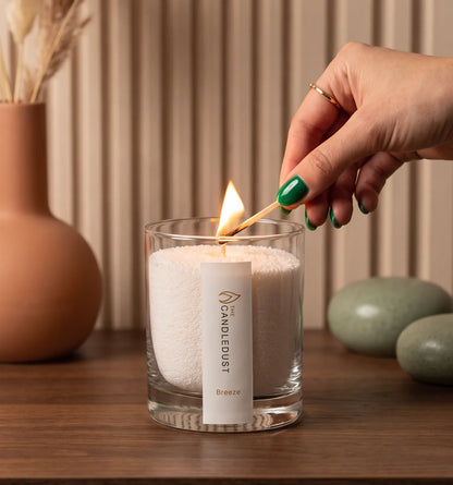 Close-up of a woman's hand lighting the cotton wick of a Breeze scented pearled sand candle in glass