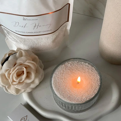Candledust Dark Honey scented pearled Candle sand with a lit wick, surrounded by decorative elements on a light surface.