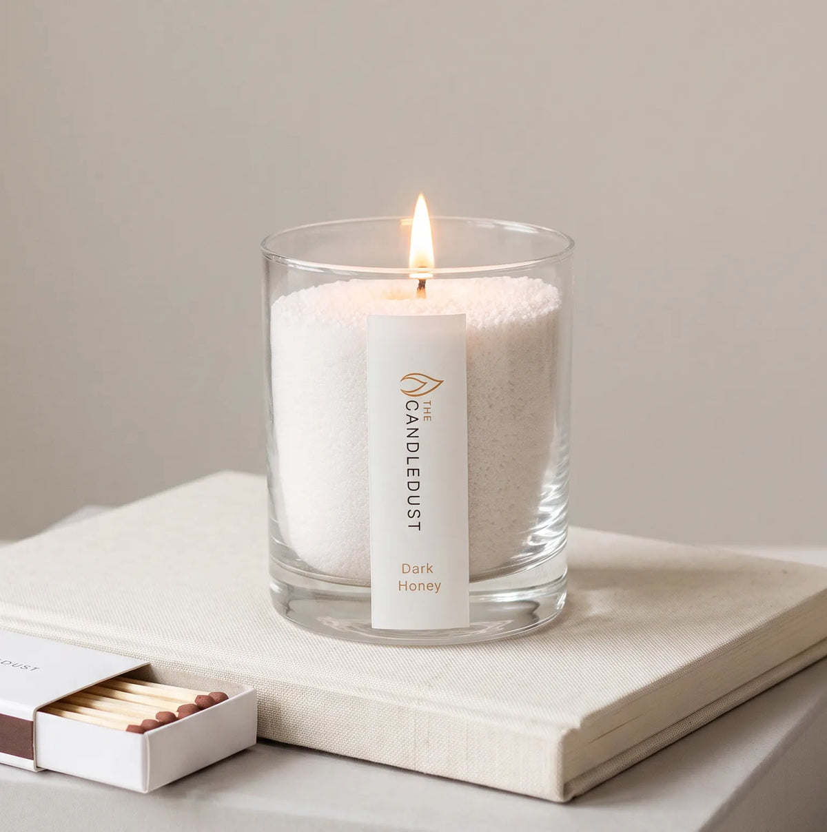 Lit Dark Honey scented pearled glass candle displayed resting on a book