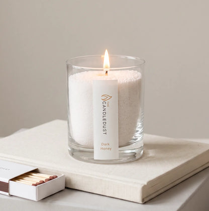Lit Dark Honey scented pearled glass candle displayed resting on a book