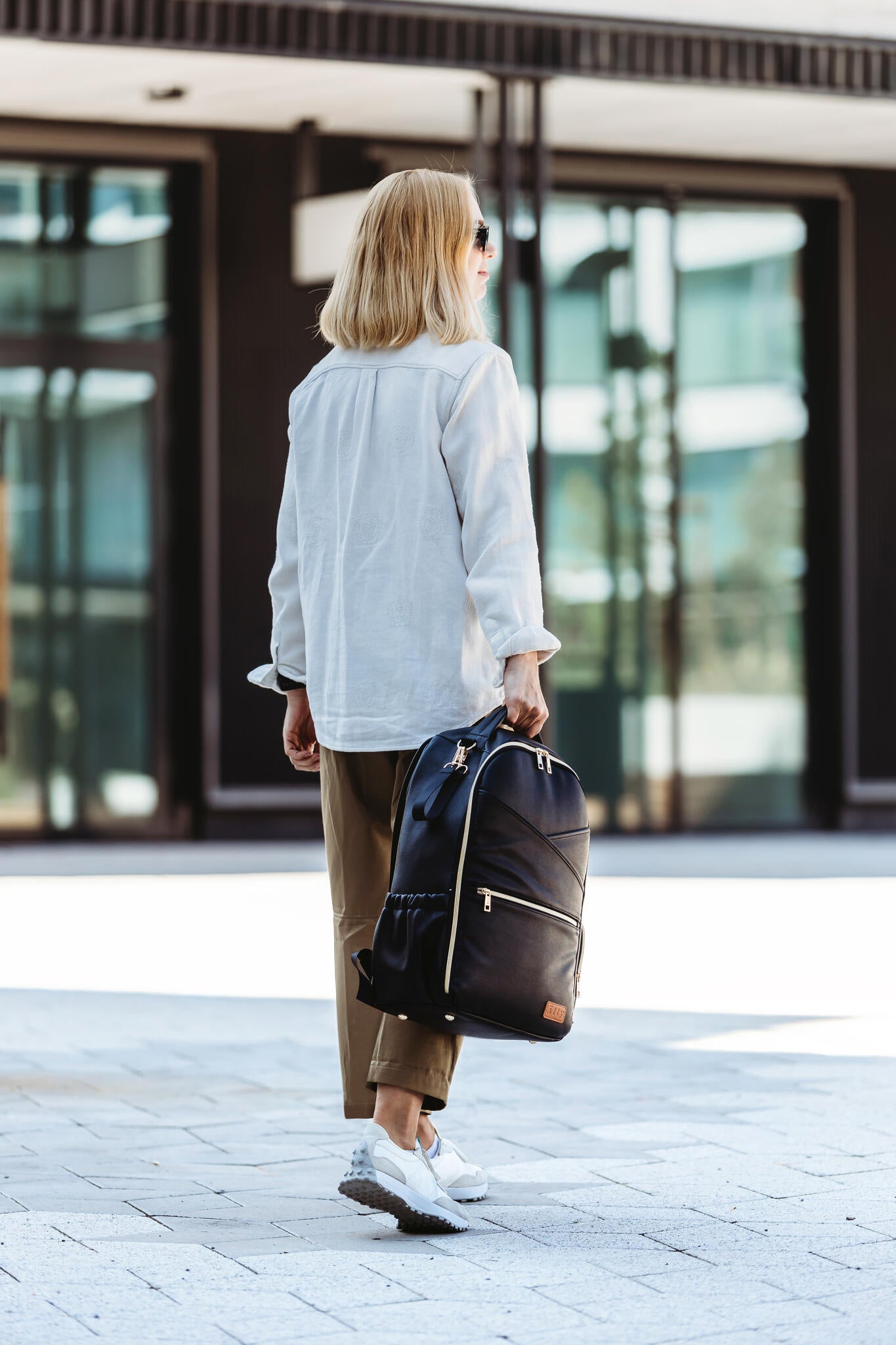 Model holding the Large Espresso Backpack by the top handle