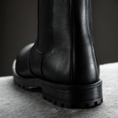 Black leather boot on a gray surface with a dark background