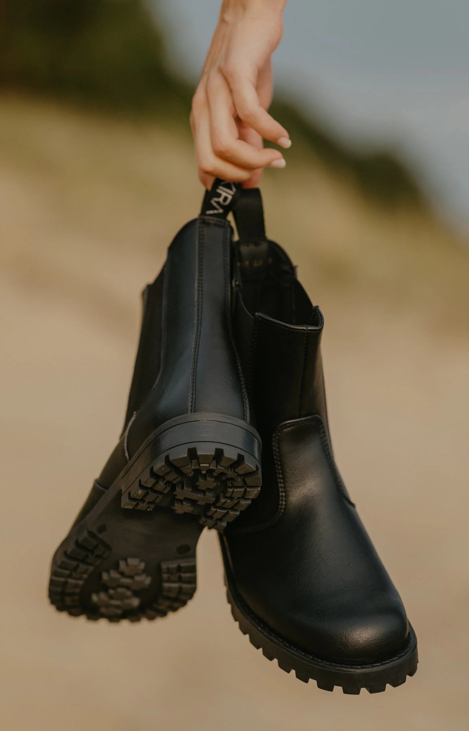 Black boots held by a hand against a blurred natural background