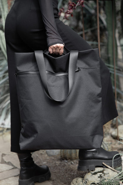 Model holding VIK Large Tote Bag by top handles with one hand outdoors, spacious laptop tote