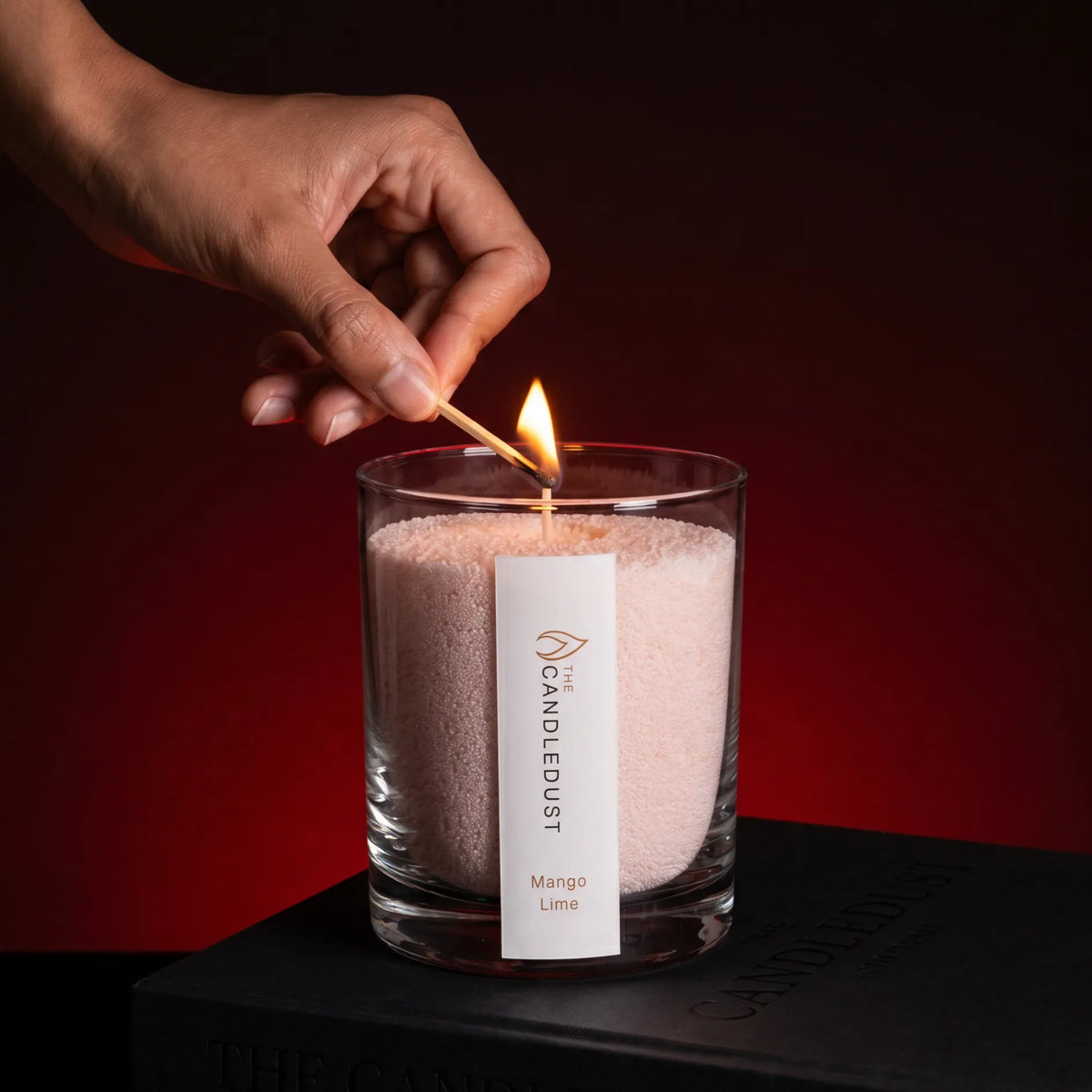 Close-up of a woman's hand lighting the cotton wick of a Mango Lime scented pearled sand candle in glass