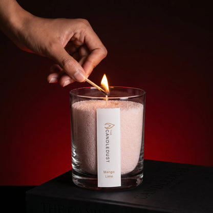 Close-up of a woman's hand lighting the cotton wick of a Mango Lime scented pearled sand candle in glass