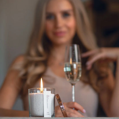 Lit Candledust Nordic Lights scented pearled candle with an elegant woman holding a glass of wine in the background