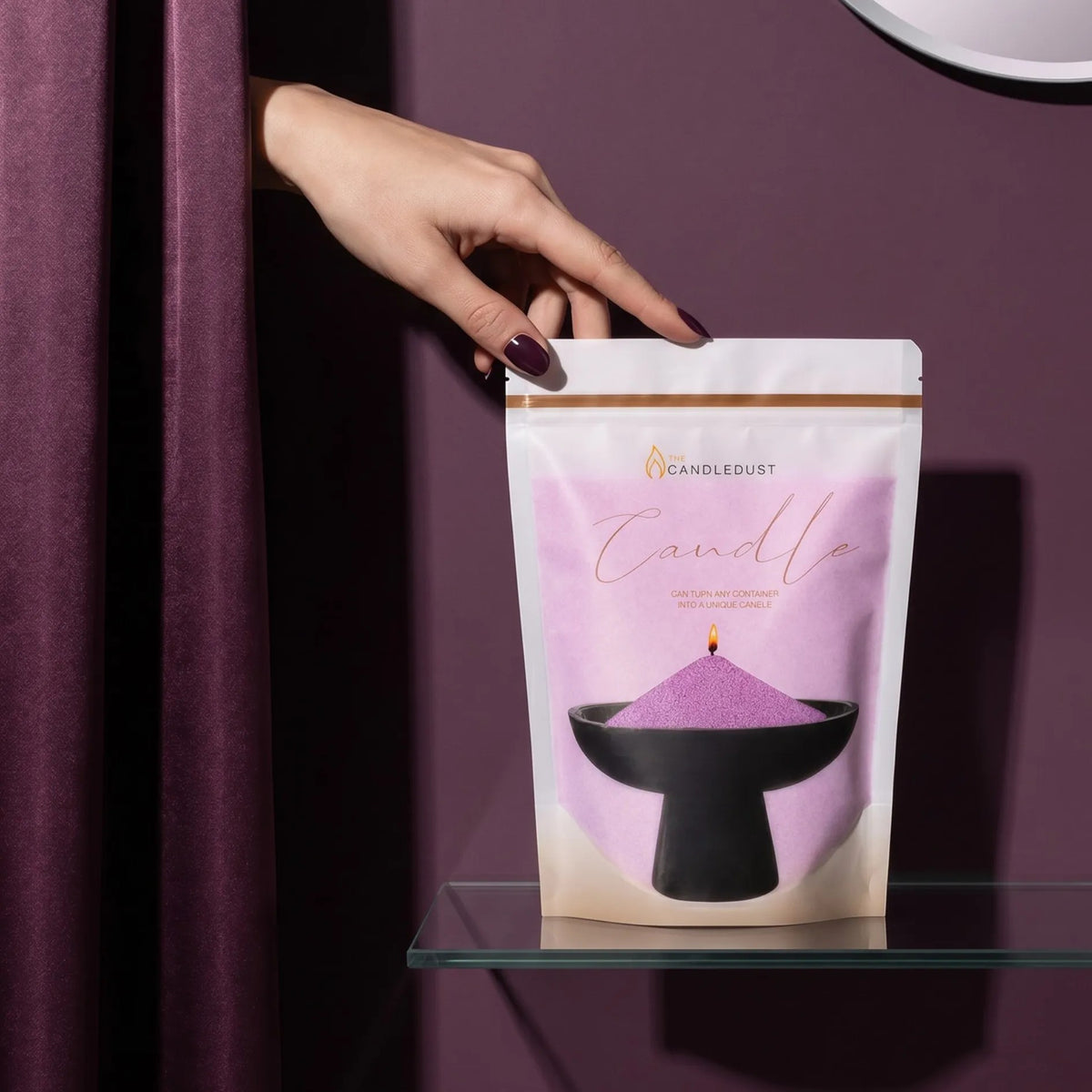 Woman's hand reaching from behind an amethyst purple curtain to touch a 1kg pearled candle sand refill pouch on a glass shelf
