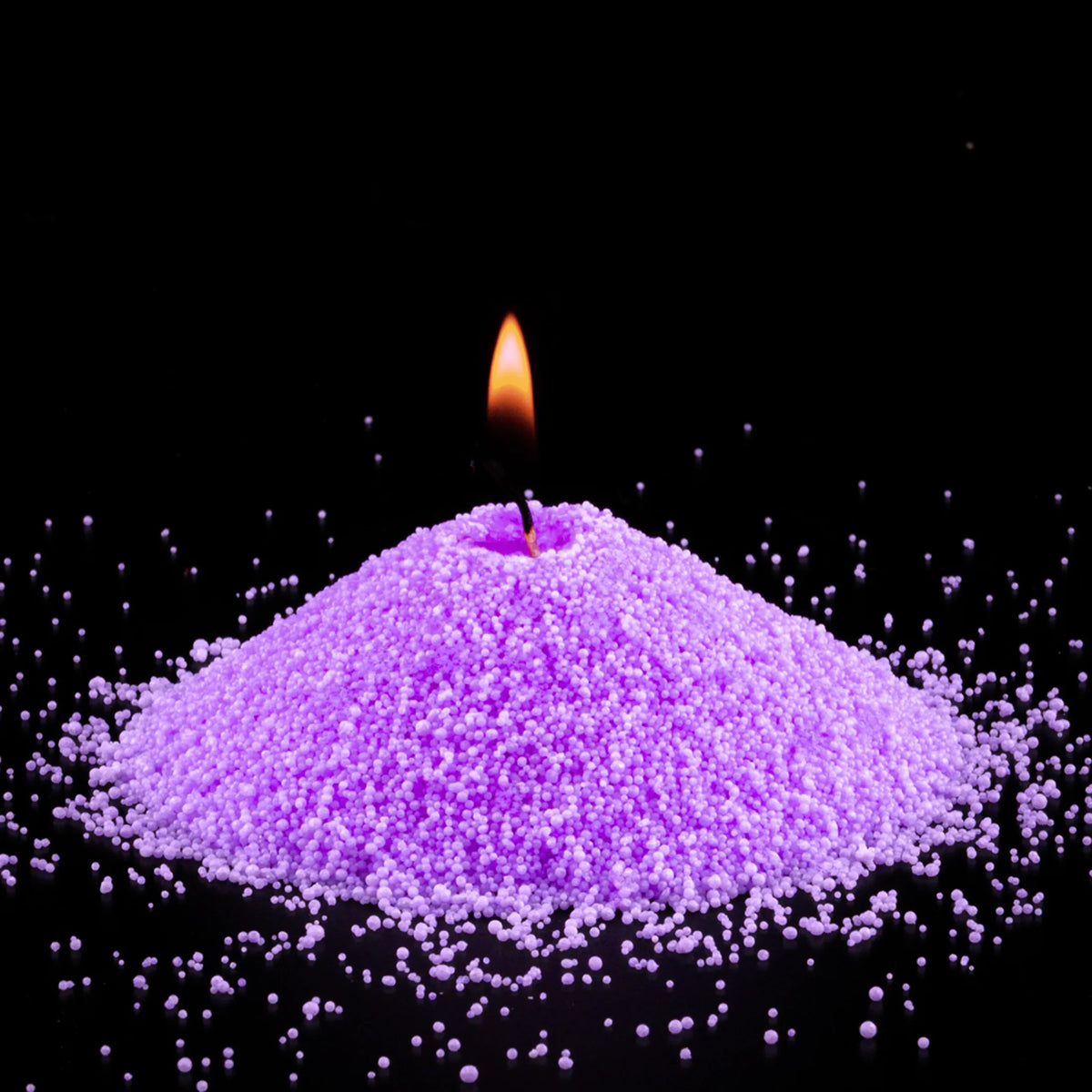 Burning Amethyst pearled sand candle with a bright flame isolated on a dramatic black background