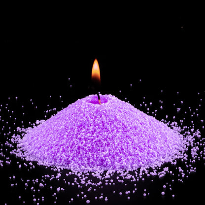 Burning Amethyst pearled sand candle with a bright flame isolated on a dramatic black background