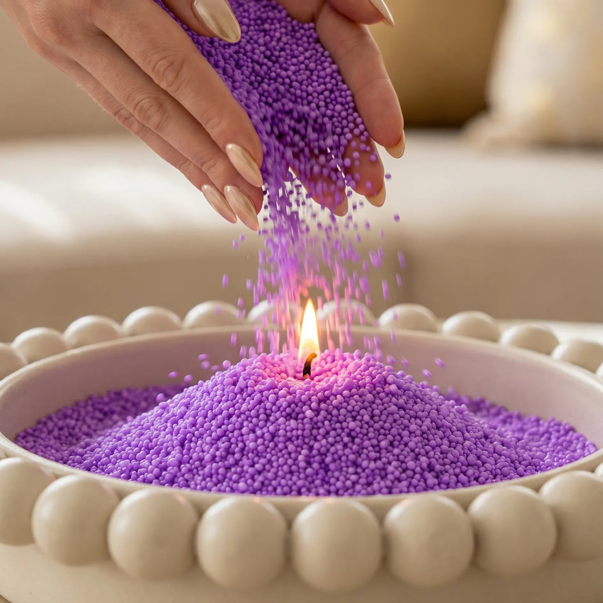 Woman pouring Amethyst pearled candle sand into an elegant tray with one already lit wick burning