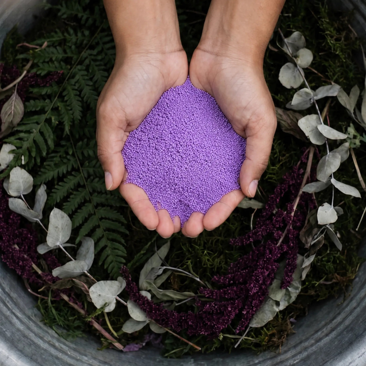 Amethyst pearled candle wax granules held in cupped hands over a garden planter vase