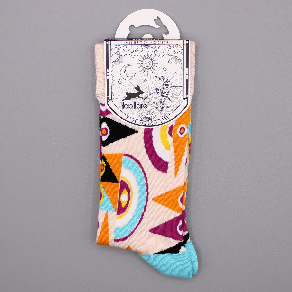 Folded Hop Hare Psychedelic Evil Eye bamboo socks with original paper sleeve packaging on a smooth gray background