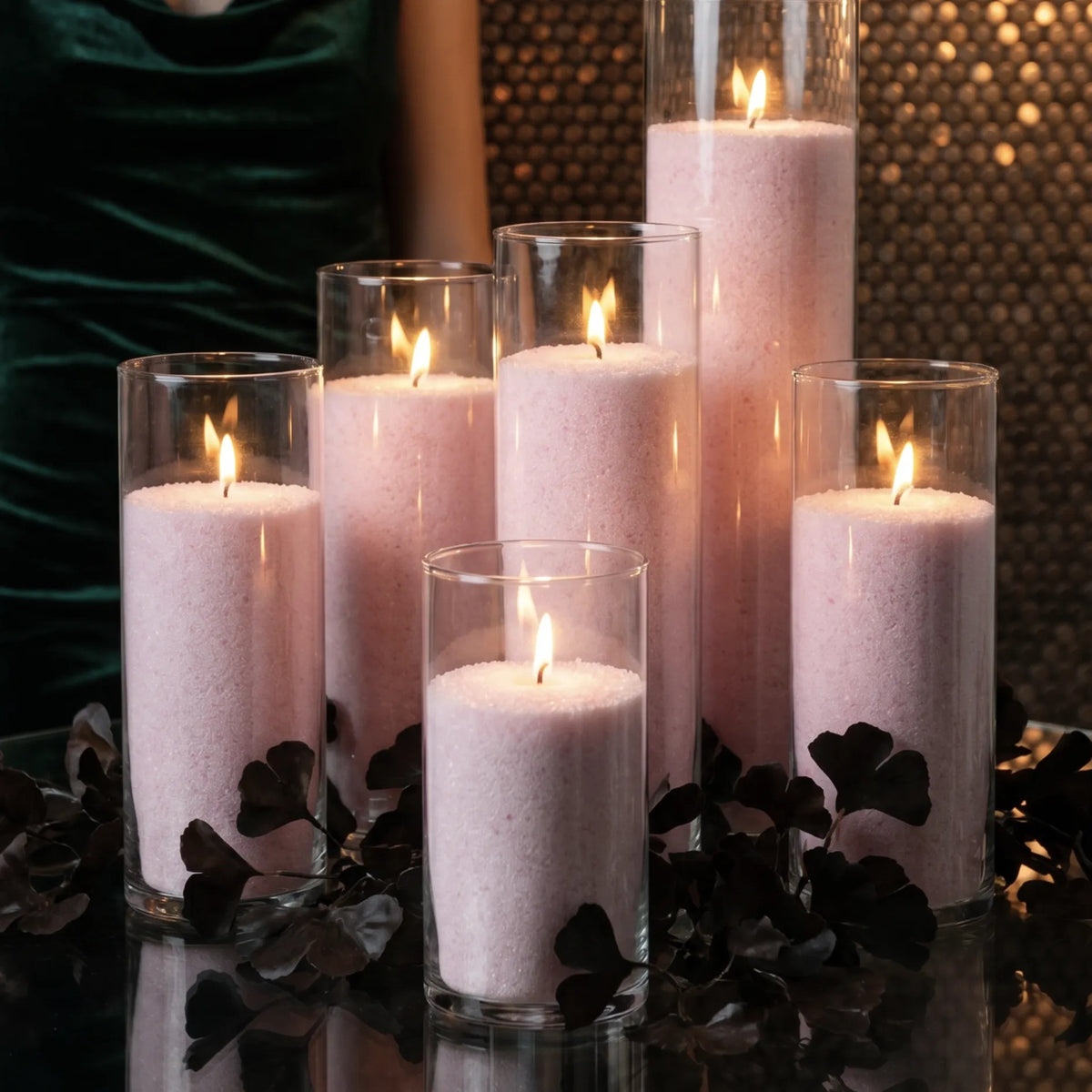Six glass vases of various heights filled with burning Baby Pink pearled candle sand creating a glowing cluster