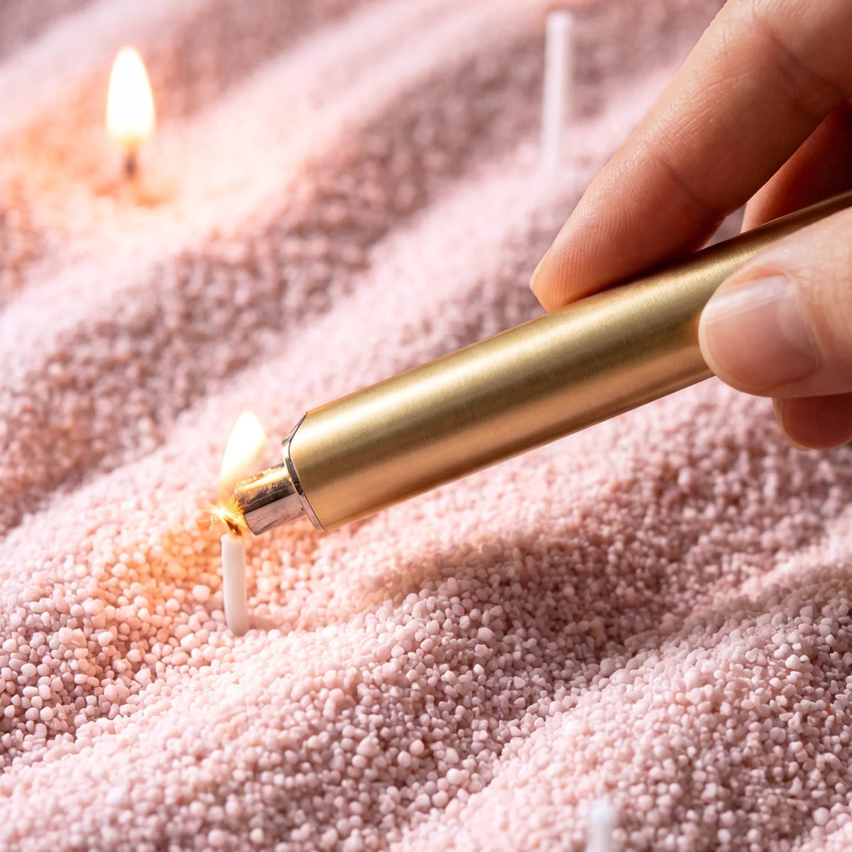 Close-up of a woman's hand lighting the cotton wick of a Baby Pink pearled sand candle
