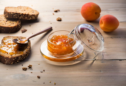 La Rochère clear Bee glass butter dish used to serve fresh apricot jam, placed on a wooden breakfast table