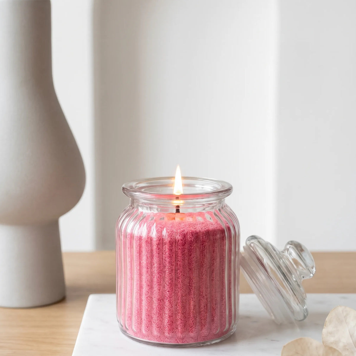 Elegant glass vase filled with Blush Vintage pearled candle sand and lit cotton wicks resting on a refined wooden countertop