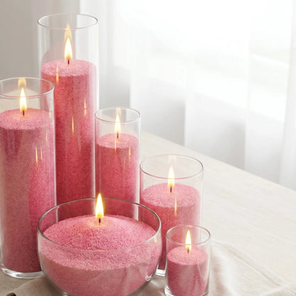 Six glass vases of various heights filled with burning Blush Vintage pearled candle sand creating a glowing cluster
