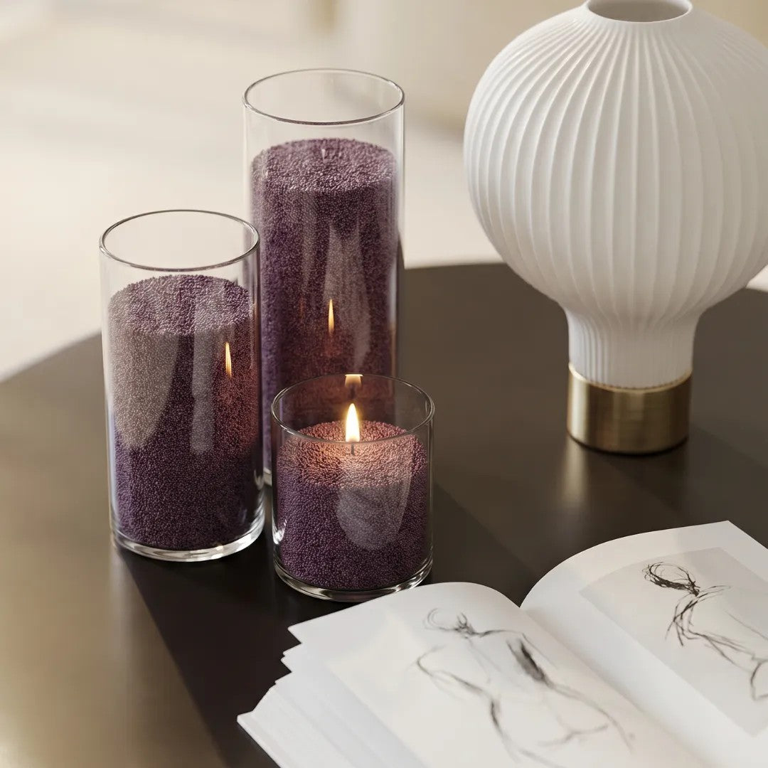 Three glass vases of various heights filled with burning Dark Lilac pearled candle sand creating a glowing cluster