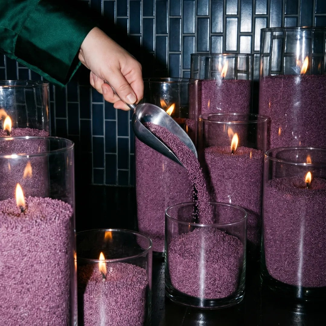 Woman filling decorative glass candle holders with Dark Lilac natural pearled candle sand