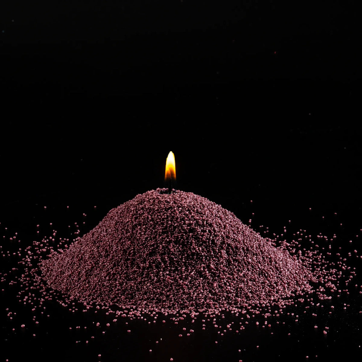 Burning Dark Lilac pearled sand candle with a bright flame isolated on a dramatic black background