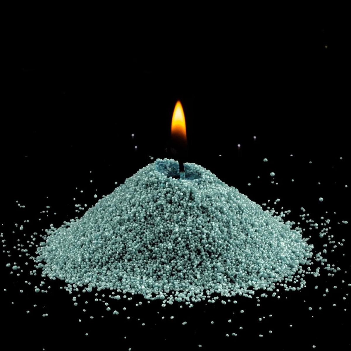 Burning Emerald pearled sand candle with a bright flame isolated on a dramatic black background