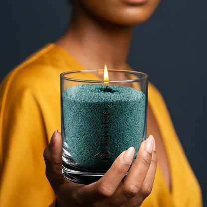 Woman holds a lit Candledust Emerald Green unscented pearled candle in a 160g glass jar