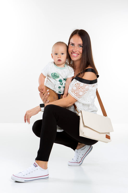 Lifestyle shot of a model with the Cappuccino handbag on a cafe table while holding her baby