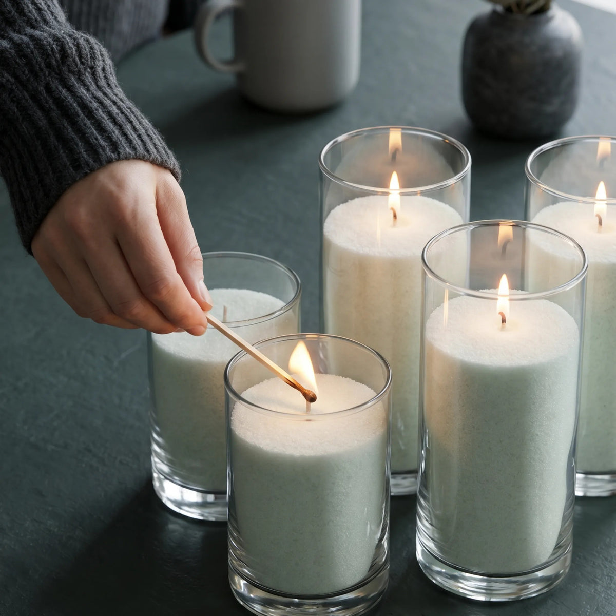 Close-up of a woman's hand lighting the cotton wick of a Lemongrass Ginger scented pearled sand candle