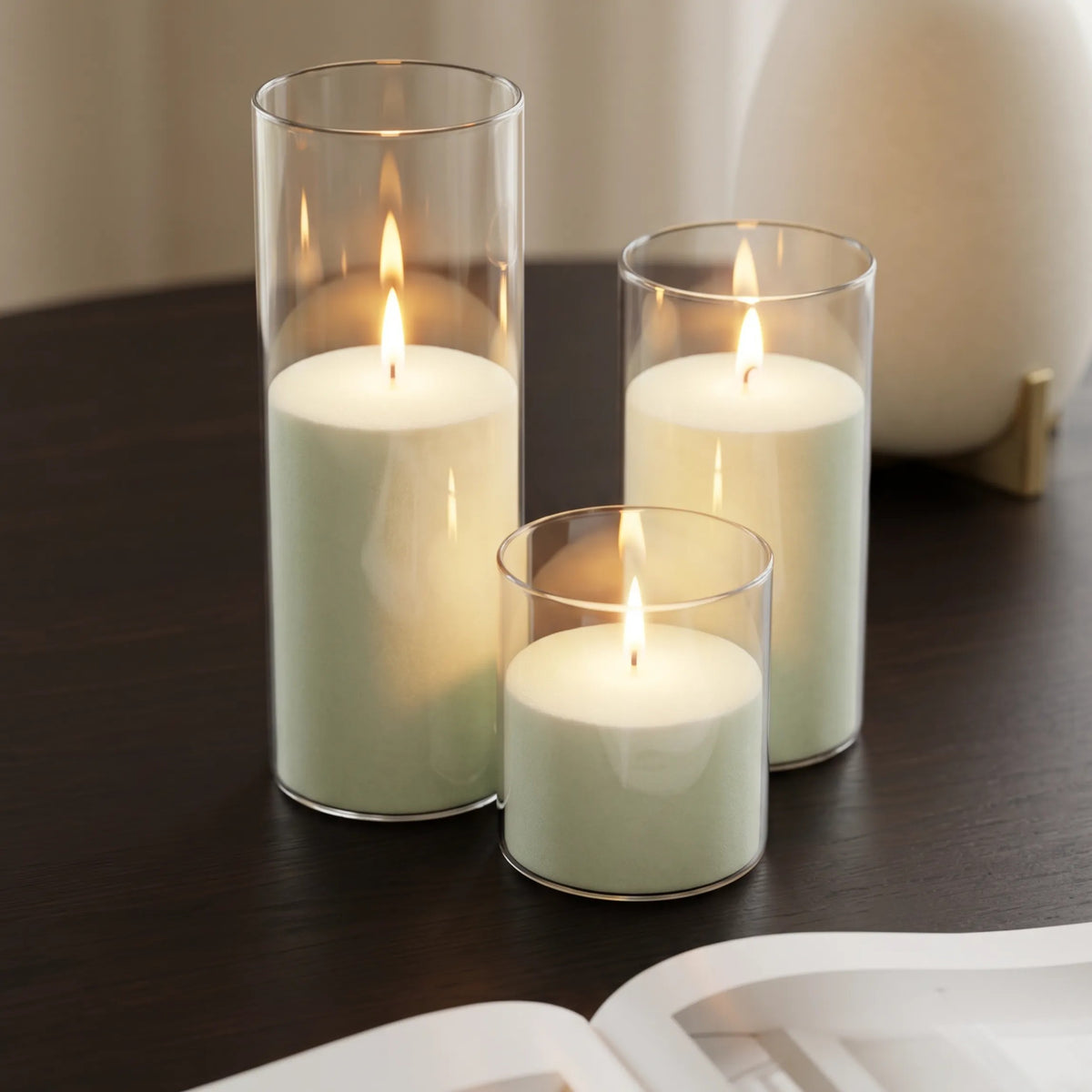 Glass candles with Lemongrass Ginger scented pearled sand and lit cotton wicks resting on a refined wooden table