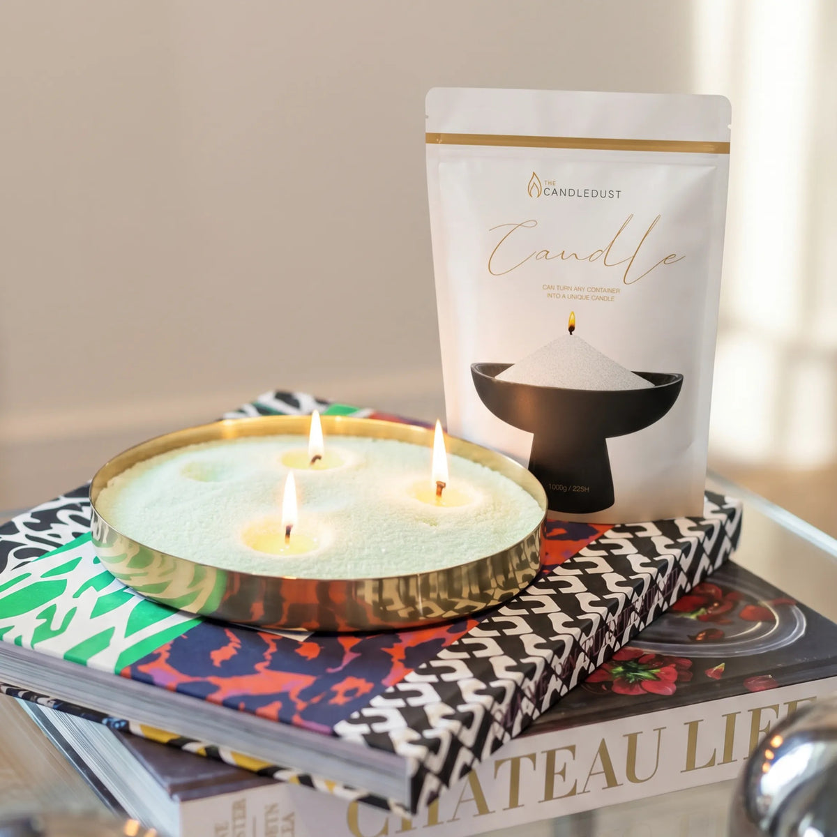 Lit Lemongrass Ginger scented pearled sand candle displayed on a decorative tray resting on stacked books