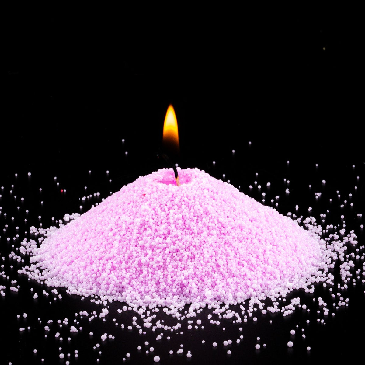 Burning Lilac pearled sand candle with a bright flame isolated on a dramatic black background