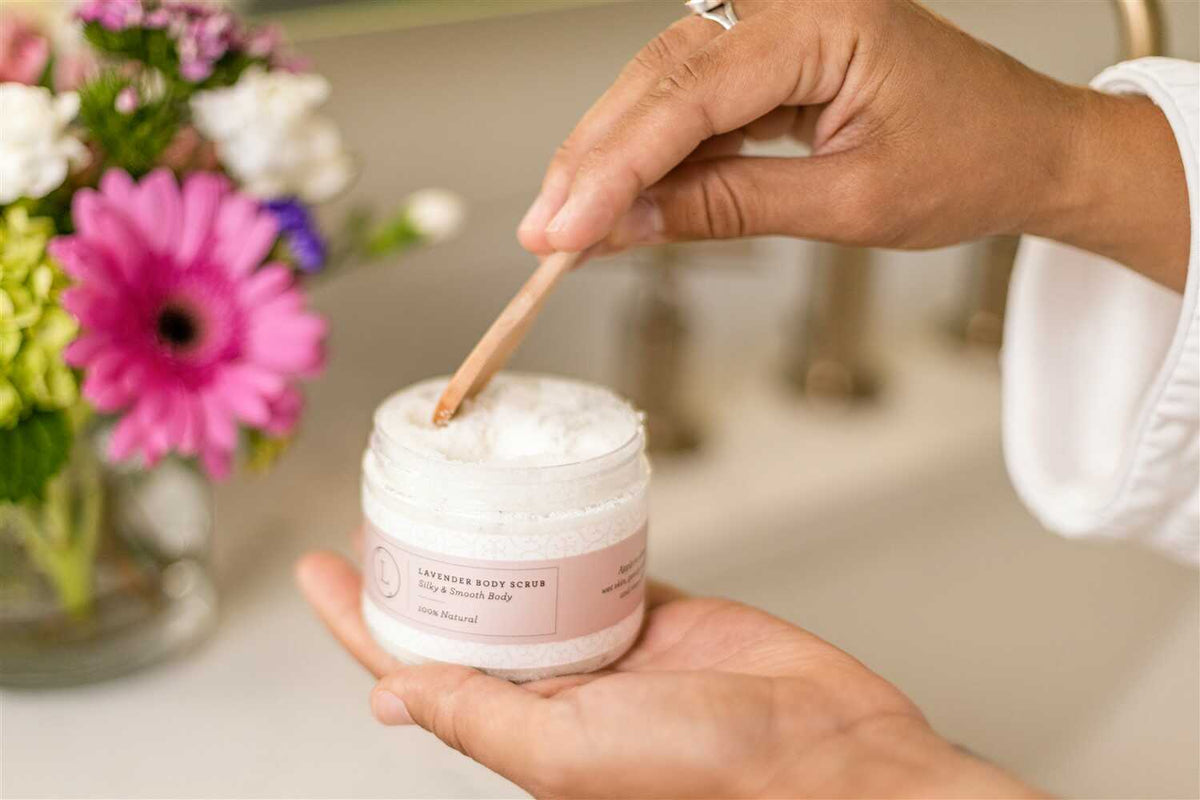 Lizush CBD Lavender Body Scrub - Woman holding jar in her palm and scooping product with a spoon in bathroom